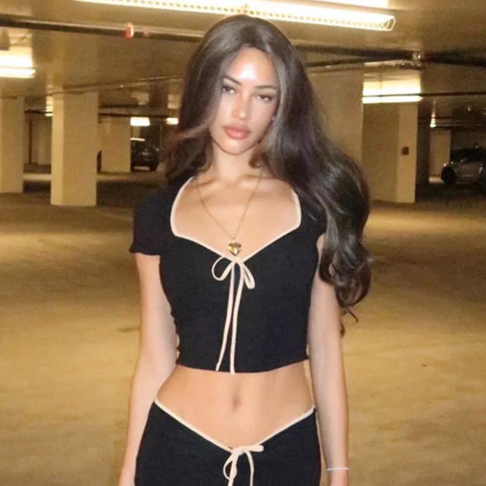 A woman wearing a black low-cut crop top with a bow detail at the neckline.