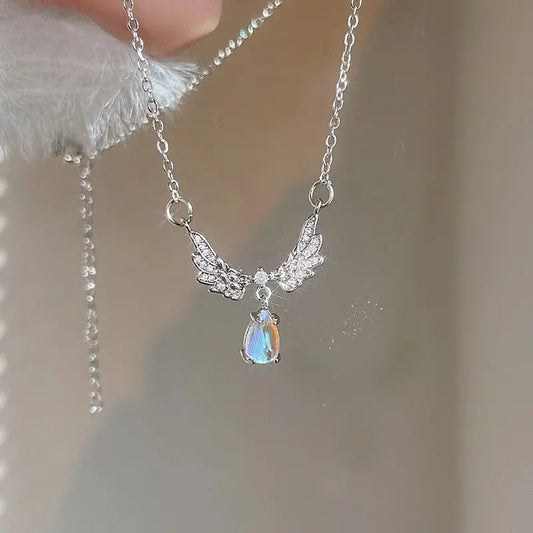 A silver-colored angel wings pendant necklace with a moonstone in the center, held between fingers.