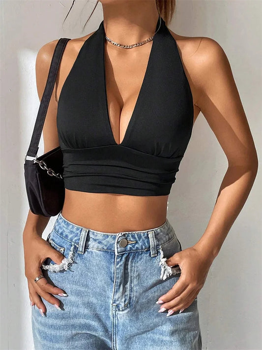 A woman wearing a black backless deep V halter crop top with a necklace and blue jeans.