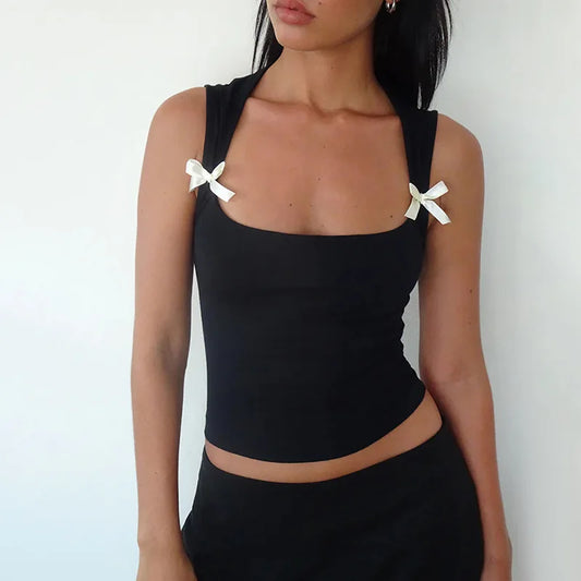 A person wearing a black bandage crop top with bow ties on the straps and a low-cut neckline.