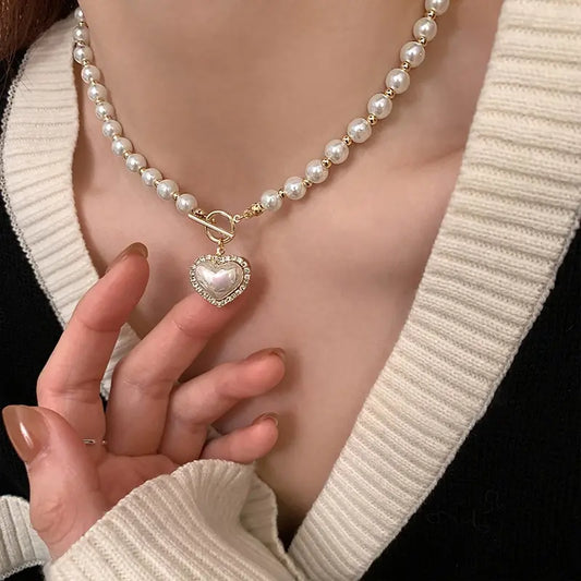 A close-up image of a woman wearing a white sweater and showcasing an elegant pearl necklace with a heart-shaped pendant.