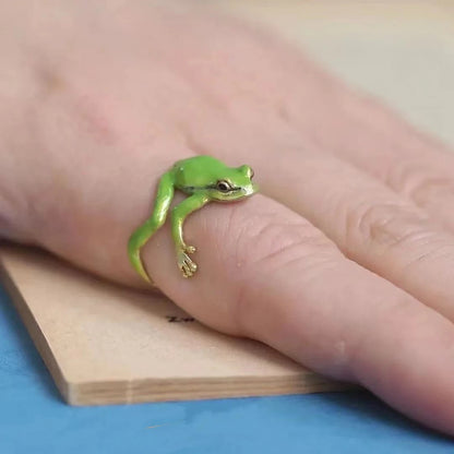 An adjustable green enamel frog ring placed on a person's finger, with the frog design facing upwards.